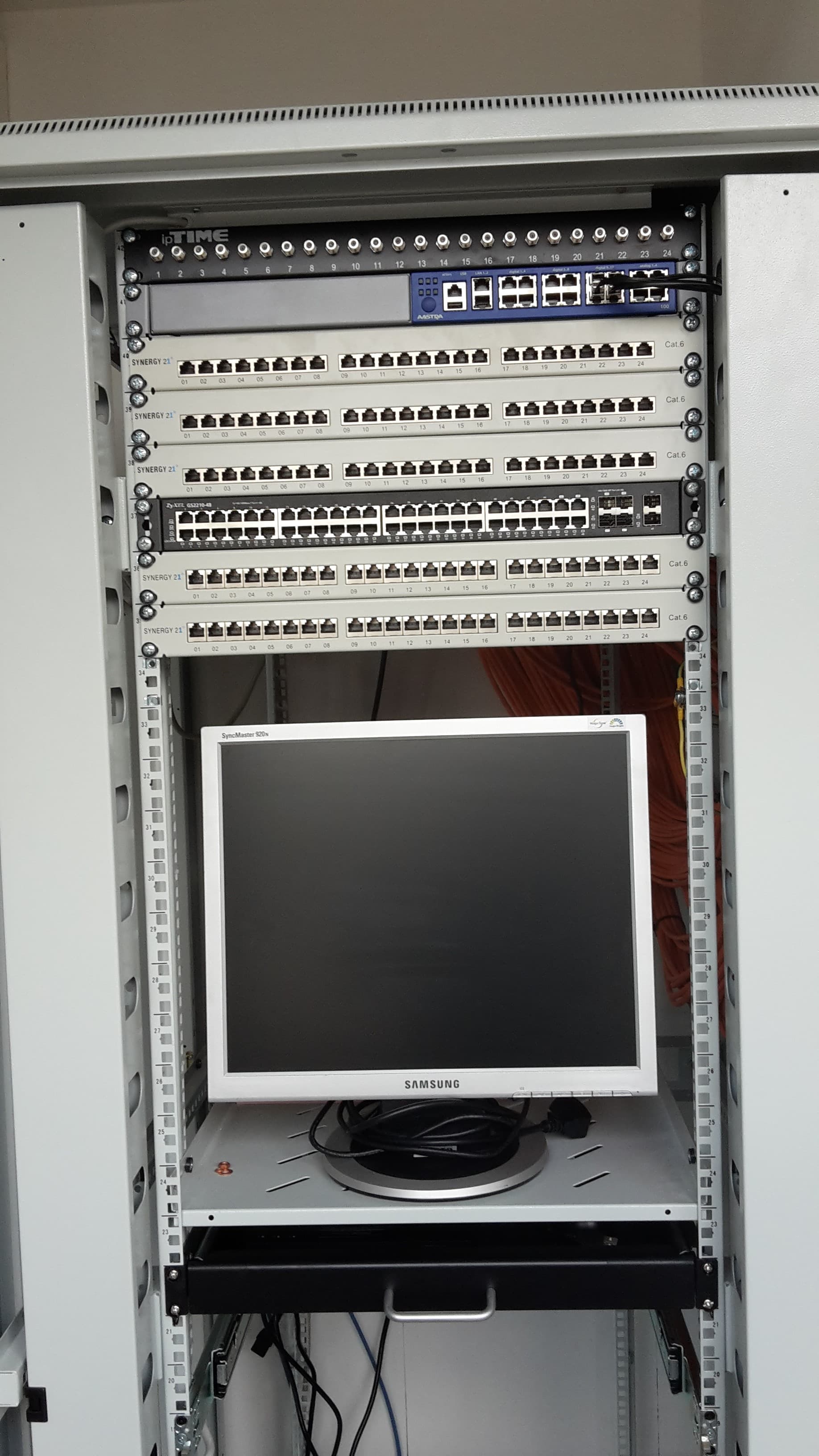 Ein Netzwerkschrank mit mehreren Patchpanels, einem Switch und einem Samsung-Monitor auf einem Fachboden.